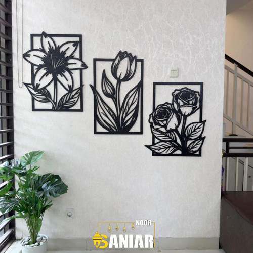 ست سه عددی تابلو دیواری مشکی طرح گلهای مختلف نصب شده به صورت پلکانی روی دیوار سفید کنار نرده راهپله».