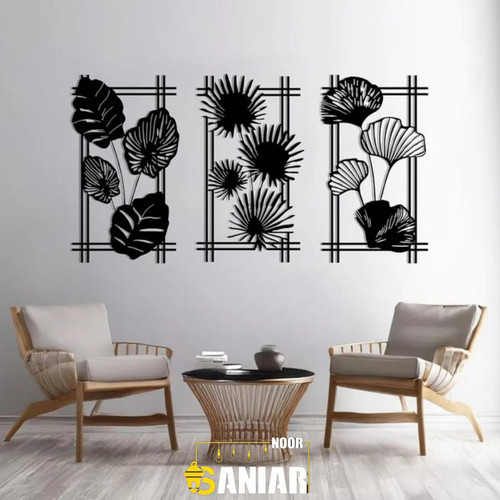 ست سه تایی تابلو دیواری مشکی طرح برگهای مختلف استوایی نصب شده روی دیوار سفید در یک اتاق نشیمن با صندلیهای مدرن».