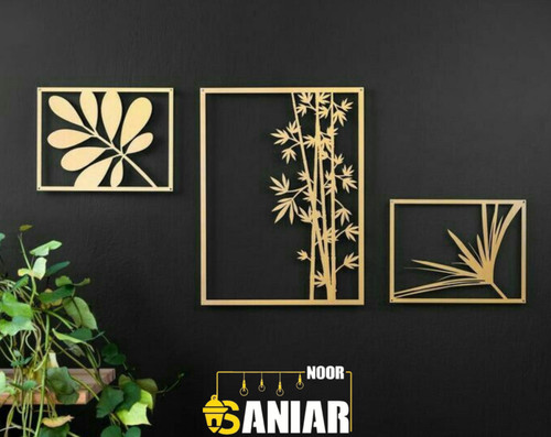 ست ۳ عددی تابلو دکوراتیو طلایی با طرحهای متنوع گیاهی شامل بامبو و برگ انجیری نصب شده روی دیوار مشکی مات در کنار گیاه طبیعی».