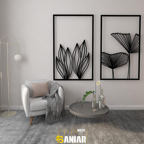 ست دو عددی تابلو مشکی فلزی با طرحهای برگ مدرن نصب شده روی دیوار طوسی روشن در کنار یک مبل تکنفره سفید و آباژور مدرن».