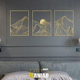 ست سه تایی تابلو دکوراتیو طلایی با طرح رشتهکوههای انتزاعی و خورشید نصب شده بر روی دیوار طوسی تیره بالای تختخواب مدرن».