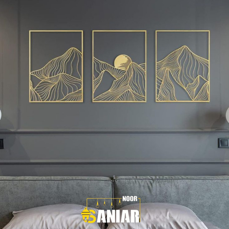 ست سه تایی تابلو دکوراتیو طلایی با طرح رشتهکوههای انتزاعی و خورشید نصب شده بر روی دیوار طوسی تیره بالای تختخواب مدرن».