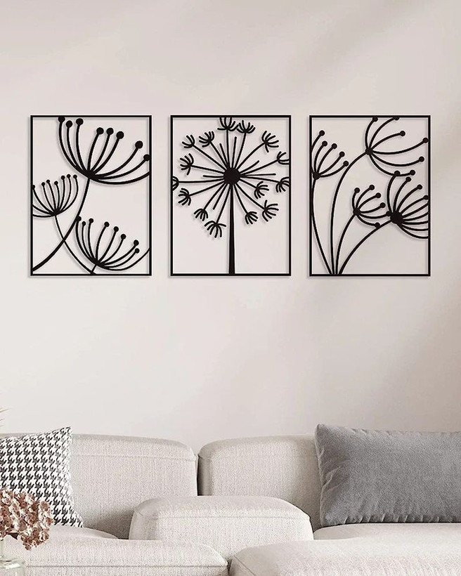 سه عدد قاب مستطیلی مشکی فلزی با طرحهای متفاوت قاصدک که به صورت همسطح و موازی روی دیوار کرم بالای مبل نصب شدهاند».