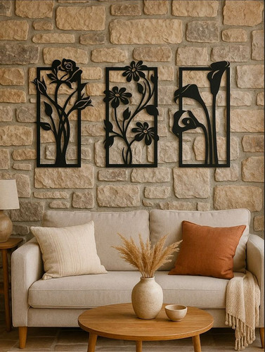 سه عدد قاب مستطیلی مشکی فلزی با طرحهای مختلف گل که به صورت متقارن روی دیوار سنگی بالای کاناپه کرم نصب شدهاند».