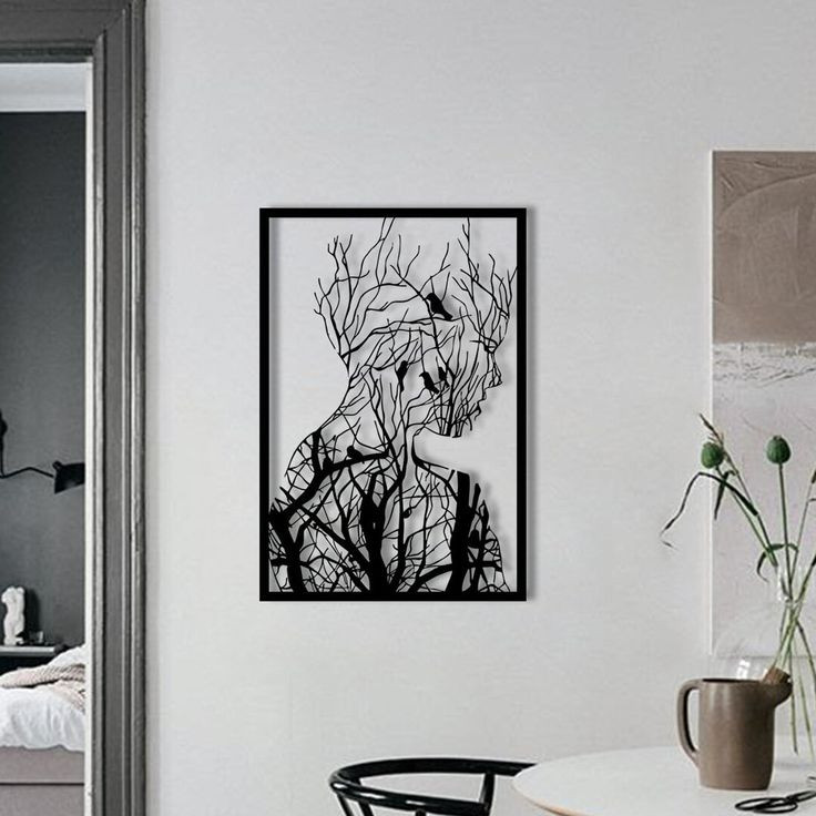 تابلو فلزی مستطیلی مشکی با طرح نیمرخ انسان که با شاخههای درخت و پرندگان ترکیب شده است، نصب شده روی دیوار سفید اتاق».