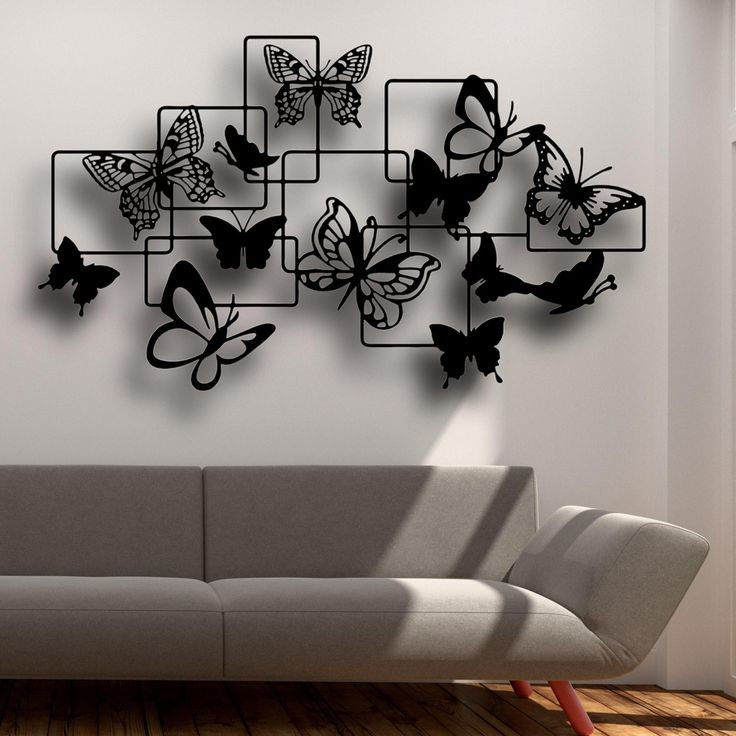 دیوارکوب بزرگ فلزی مشکی با طرح پروانههای متنوع در میان کادرهای مربعی درهمتنیده، نصب شده روی دیوار سفید اتاق نشیمن».