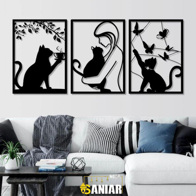 «ست سه تایی قاب فلزی مشکی با طرحهای گربه در حال نوشیدن قهوه، گربه در آغوش دختر و گربه در حال بازی با پروانهها، نصب شده روی دیوار سفید بالای کاناپه مدرن».