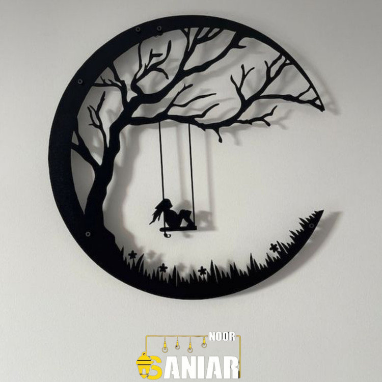 یک دیوارکوب فلزی گرد مشکی با طرح دختری که روی یک تاب آویزان از شاخه درخت در میان هلال ماه نشسته است، نصب شده روی دیوار سفید اتاق خواب».
