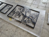 یک تابلو فلزی مشکی بزرگ با طرح شاخه و برگهای ژینکو، نصب شده روی دیوار کرم روشن در فضای بالای یک میز کنسول چوبی مدرن».