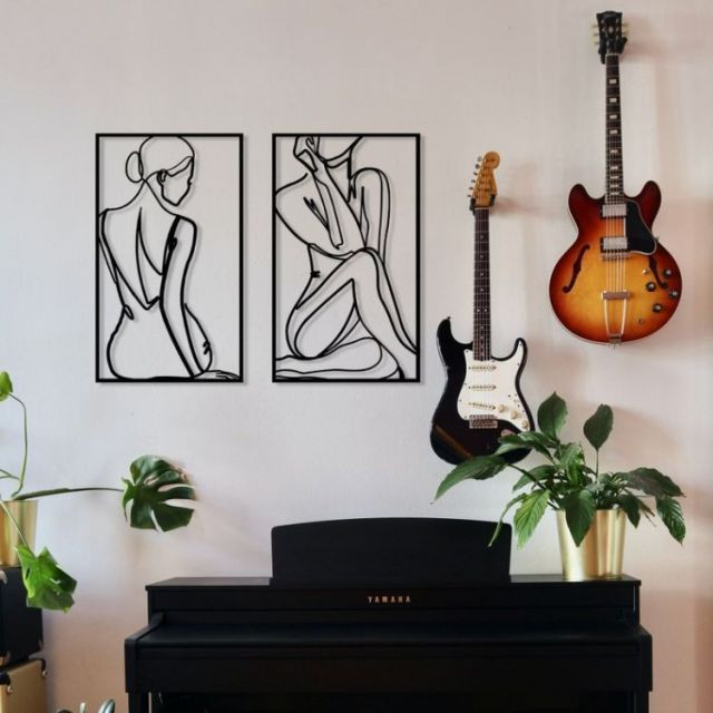 دو عدد تابلو فلزی مشکی با طرح خطی فیگور زن که بالای یک پیانو مشکی و کنار گیتار الکتریک روی دیوار نصب شدهاند.»