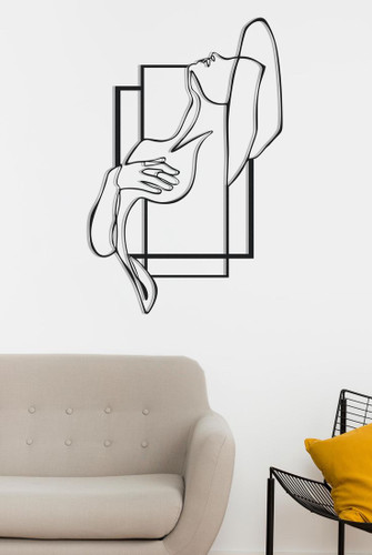 یک تابلو فلزی مشکی با طرح انتزاعی از بدن یک زن که با دو قاب مستطیلی متقاطع ترکیب شده و روی دیوار سفید بالای مبل نصب شده است.»